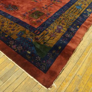 Reddish-orange rug field and multi-layered border featuring gold and navy botanical patterns on wood flooring.