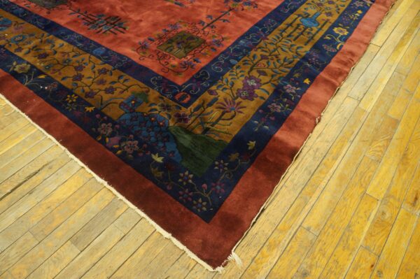 Reddish-orange rug field and multi-layered border featuring gold and navy botanical patterns on wood flooring.