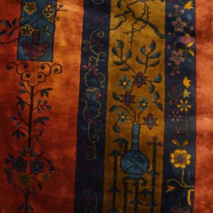 Rust, gold, and dark blue striped rug with ornate floral and botanical patterns on yellow wood floors.