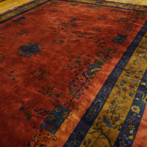 Deep rust rug featuring blue and gold floral patterns and a wide patterned border on light wood flooring.