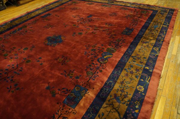 Deep rust rug featuring blue and gold floral patterns and a wide patterned border on light wood flooring.