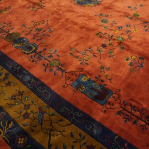 Velvety rust rug featuring blue and yellow florals, framed by patterned navy blue and golden brown borders.