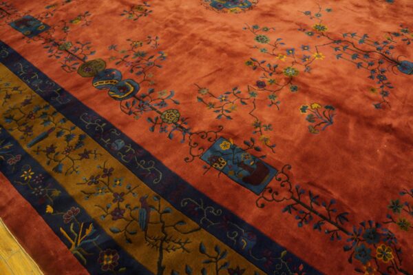 Velvety rust rug featuring blue and yellow florals, framed by patterned navy blue and golden brown borders.