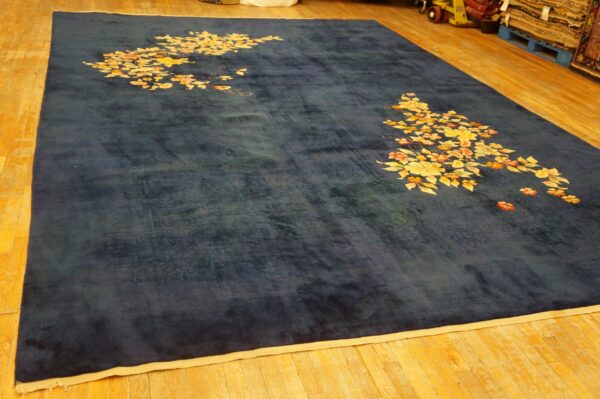 Dark blue rug with corner clusters of yellow and orange flowers on a wood floor.