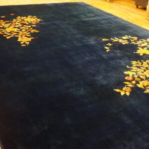 Dark blue rug with gold and orange floral patterns lies on light-colored rustic wooden flooring.