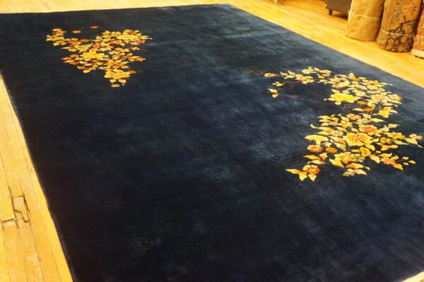 Dark blue rug with gold and orange floral patterns lies on light-colored rustic wooden flooring.