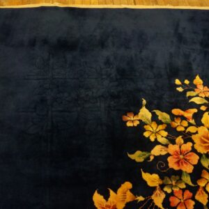 A velvety dark blue rug displays a diagonal spray of vivid orange and yellow flowers on wood flooring.