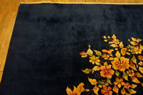 A velvety dark blue rug displays a diagonal spray of vivid orange and yellow flowers on wood flooring.