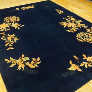 Navy blue area rug featuring stylized golden floral sprigs and vines rests on a plank wood floor.