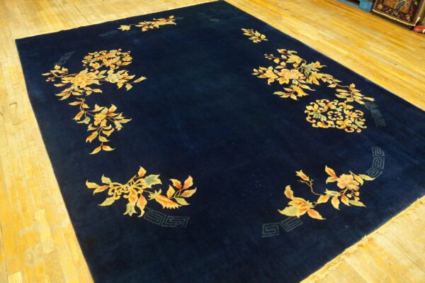 Navy blue area rug featuring stylized golden floral sprigs and vines rests on a plank wood floor.