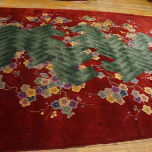 Deep red rug with multicolor flowers and a large central dark green zig-zag pattern on a wood floor.
