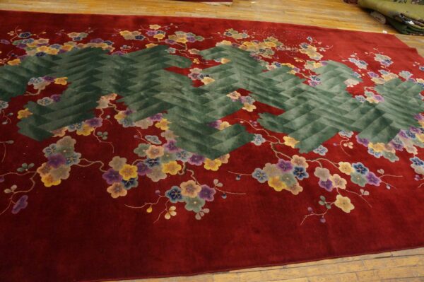 Deep red rug with multicolor flowers and a large central dark green zig-zag pattern on a wood floor.
