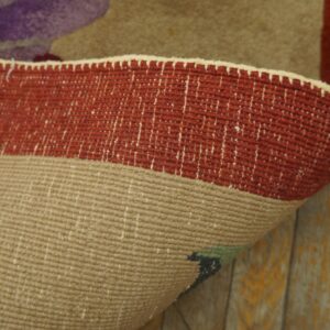 Rolled rug edge displays a flatwoven beige backing against the red border and yellow distressed wood floor.