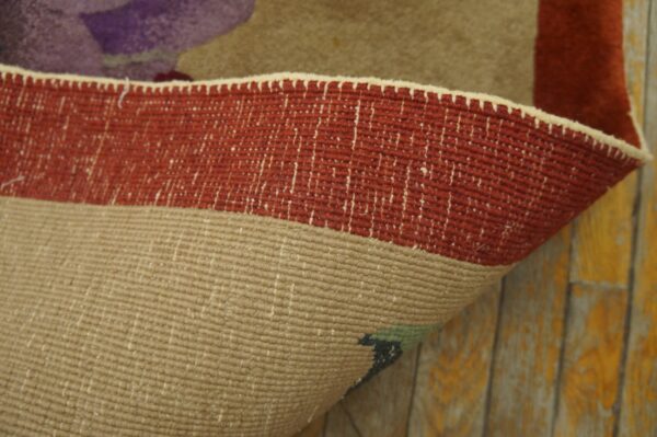 Rolled rug edge displays a flatwoven beige backing against the red border and yellow distressed wood floor.