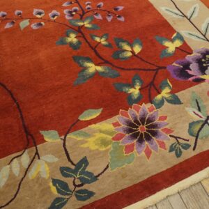 Rust and beige border rug featuring large purple, pink, and green stylized flowers on wood floor.