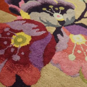Close-up of a plush rug featuring large red, purple, and pink floral designs on a light beige background.