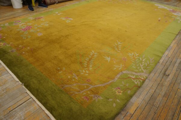 Gold oriental rug with floral and vine patterns, featuring a wide green border on hardwood floors.