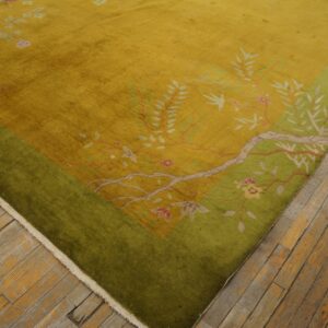 Golden yellow rug with a green border and pink floral patterns lies on worn wood plank flooring.