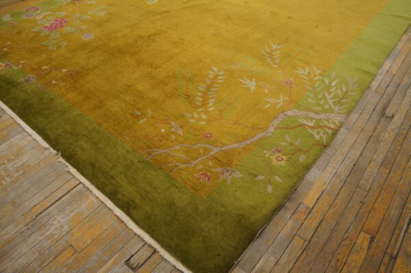 Golden yellow rug with a green border and pink floral patterns lies on worn wood plank flooring.