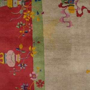 Detail of a multicolor rug showing a red floral border, a green stripe, and a light beige main field.