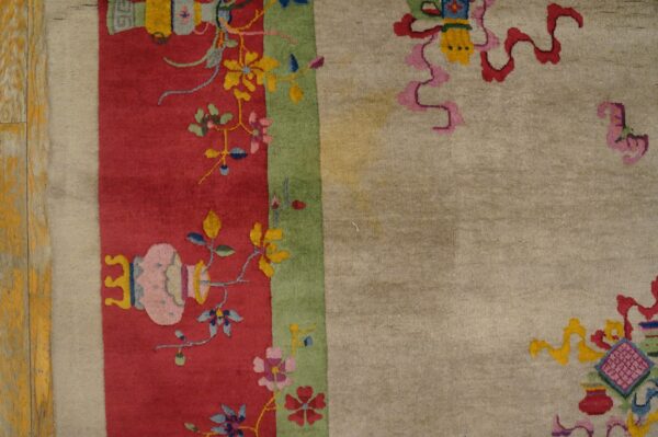 Detail of a multicolor rug showing a red floral border, a green stripe, and a light beige main field.