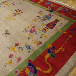 Beige rug with colorful floral, vase, and butterfly patterns, framed by wide red and green borders on wood floor.