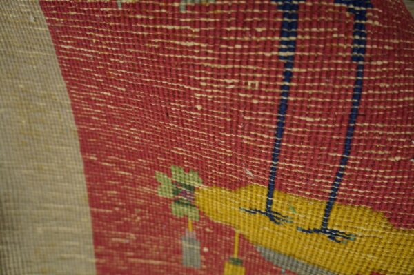 Textured, flat-woven rug detail features geometric patterns in red, yellow, beige, green, and blue.