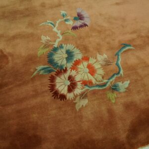 Plush salmon rug displaying a large floral cluster on distressed yellow wood flooring.