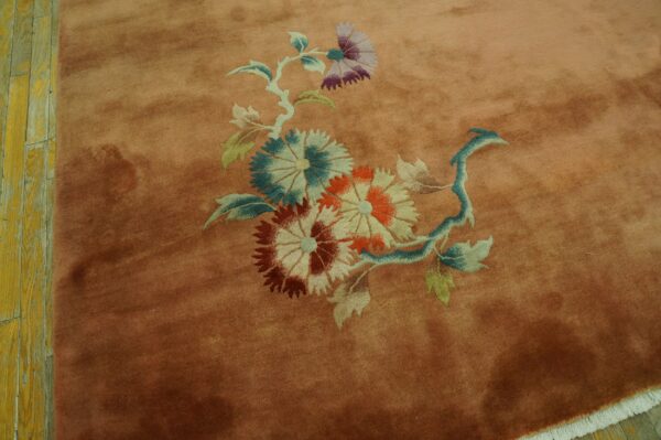 Plush salmon rug displaying a large floral cluster on distressed yellow wood flooring.