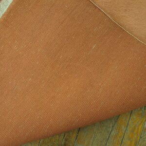 The terracotta woven backing and high pile peach surface of a rug rest upon distressed wooden planks.