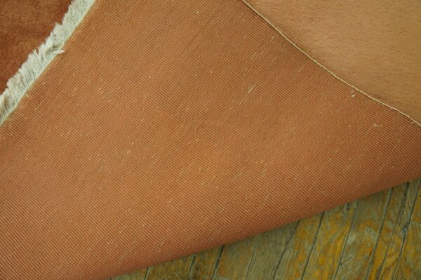 The terracotta woven backing and high pile peach surface of a rug rest upon distressed wooden planks.