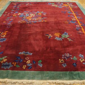 Burgundy floral rug with blue and gold accents, framed by a teal border on wooden flooring.