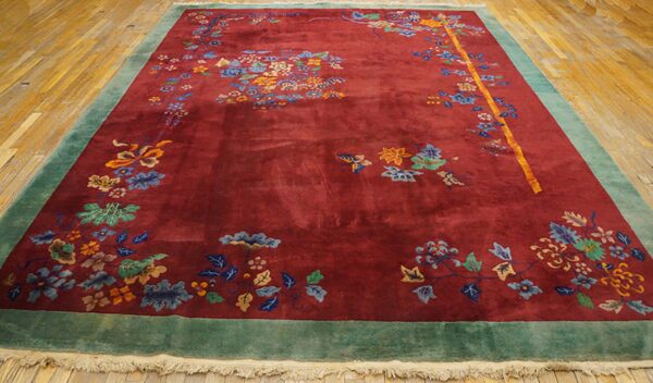Burgundy floral rug with blue and gold accents, framed by a teal border on wooden flooring.