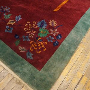 Burgundy rug with ornate floral pattern and sage green border rests on light wood planks.