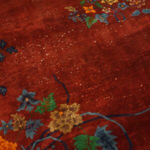 Detail view of a deep red rug with visible abrash, patterned with blue, green, and gold floral designs.