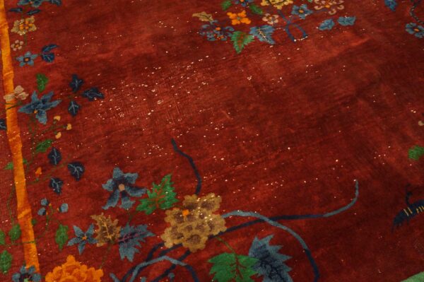 Detail view of a deep red rug with visible abrash, patterned with blue, green, and gold floral designs.