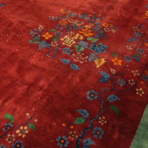 High-pile red rug with dense multicolor floral clusters and a thick green border on wood floors.
