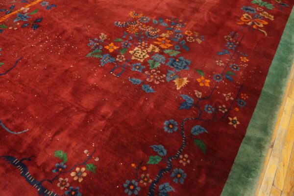 High-pile red rug with dense multicolor floral clusters and a thick green border on wood floors.