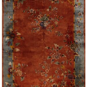 Plush rust rug featuring a complex floral and vase design centered within a wide faded blue border.
