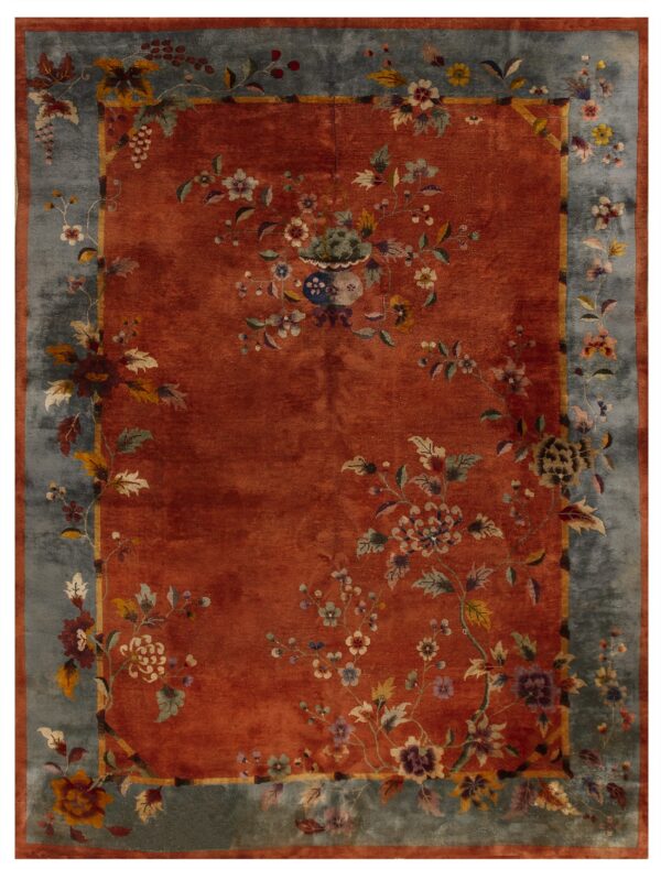 Plush rust rug featuring a complex floral and vase design centered within a wide faded blue border.