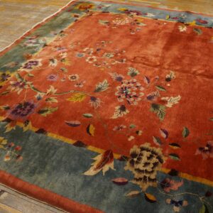 Rust orange rug with scattered multicolored floral patterns and a wide blue-green border on wood floors.