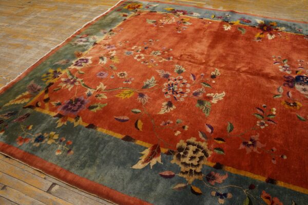 Rust orange rug with scattered multicolored floral patterns and a wide blue-green border on wood floors.
