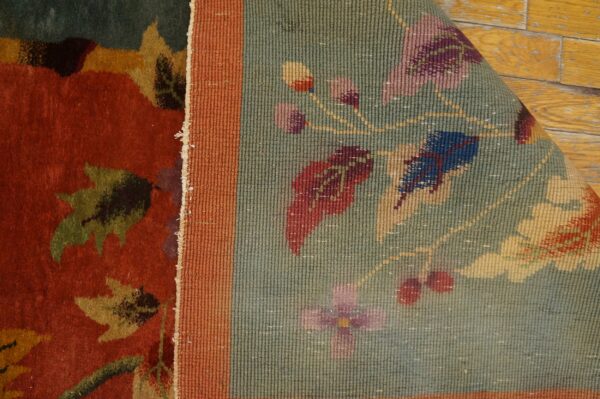 High-pile rust rug with leaves meets a ribbed sage border featuring small flowers, resting on wood.