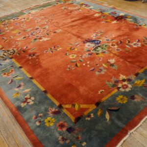 Coral-red rug featuring multi-colored floral designs and a wide teal border on distressed wooden planks.
