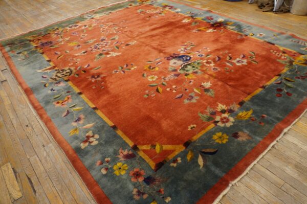 Coral-red rug featuring multi-colored floral designs and a wide teal border on distressed wooden planks.