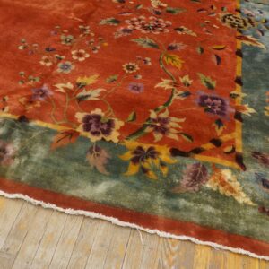 High-pile orange rug with purple and yellow floral vines, framed by a broad sage border on wood flooring.