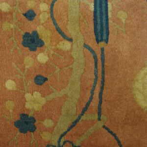 Rust rug with olive, gold, and dark blue floral motifs and a yellow lantern design next to weathered wood.