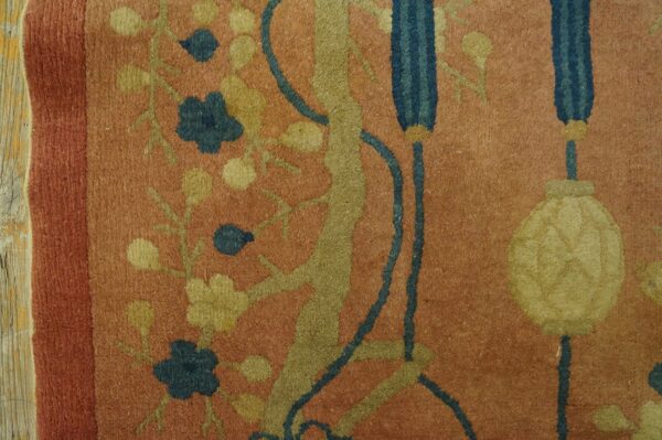 Rust rug with olive, gold, and dark blue floral motifs and a yellow lantern design next to weathered wood.