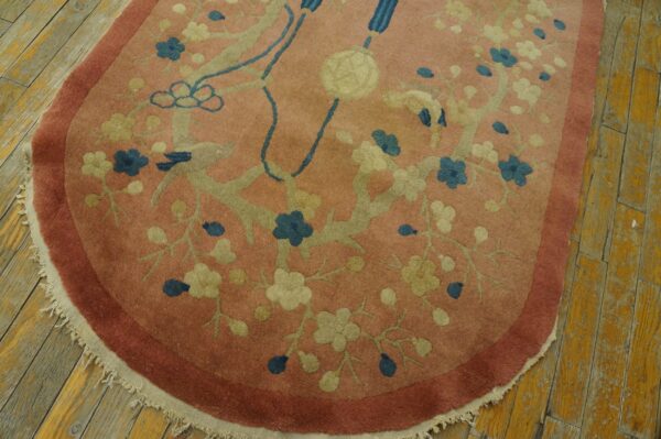 Rounded pink rug detail showing blue and cream flowers with a rose border on distressed wood.