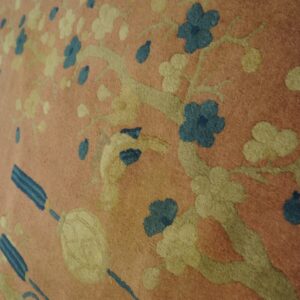 A low-pile pink rug displays a relief cut floral and branch pattern in pale yellow and deep blue.